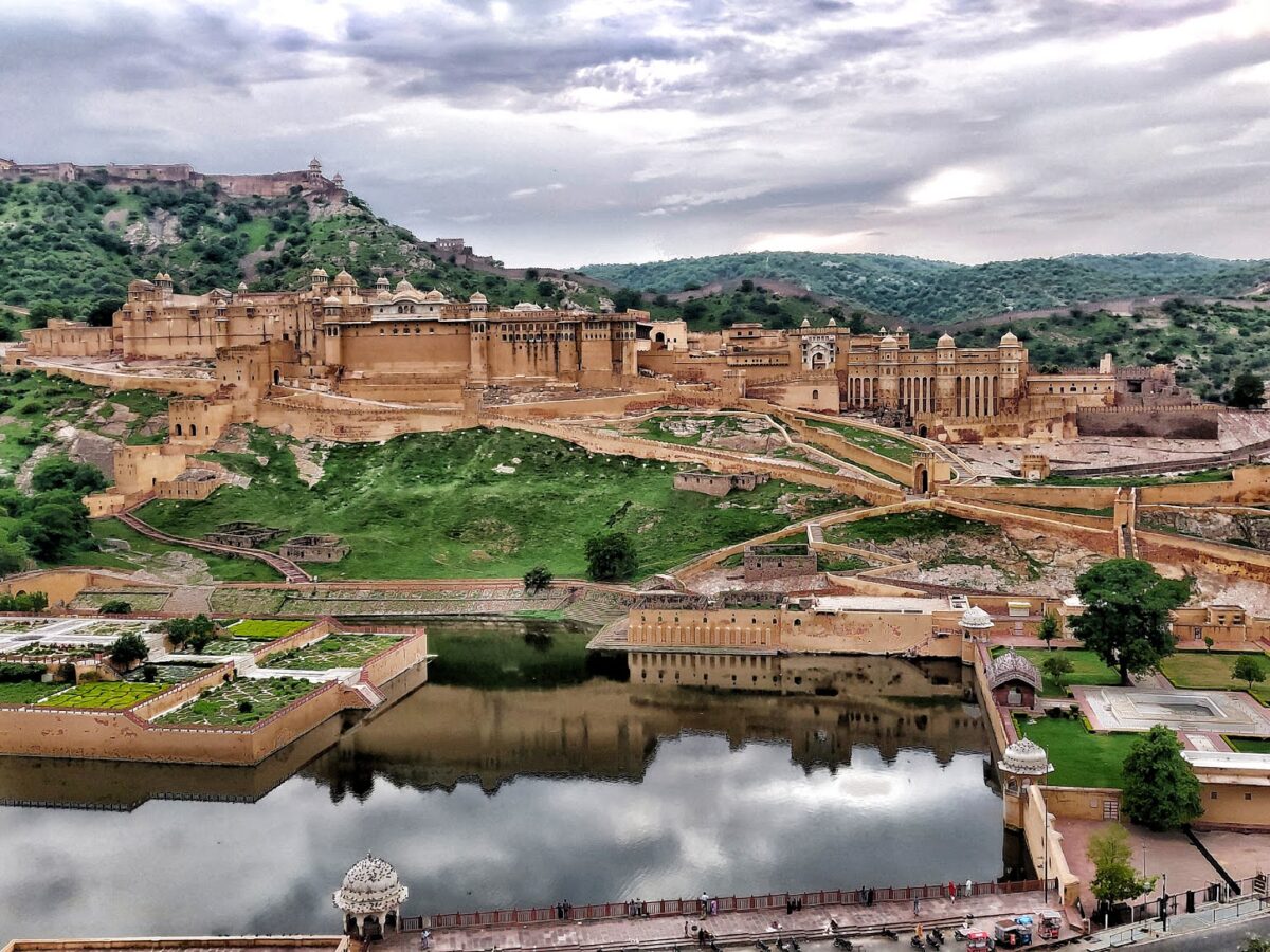 Aerial view of Amber Fort, Maota Lake, and terraced gardens in Jaipur, India under a cloudy sky.